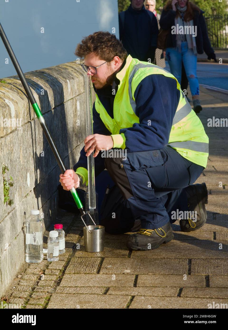Operaio in Flourescent, High Vis Jacket campionamento di acqua di fiume dal ponte sul fiume Avon, Christchurch Regno Unito Foto Stock