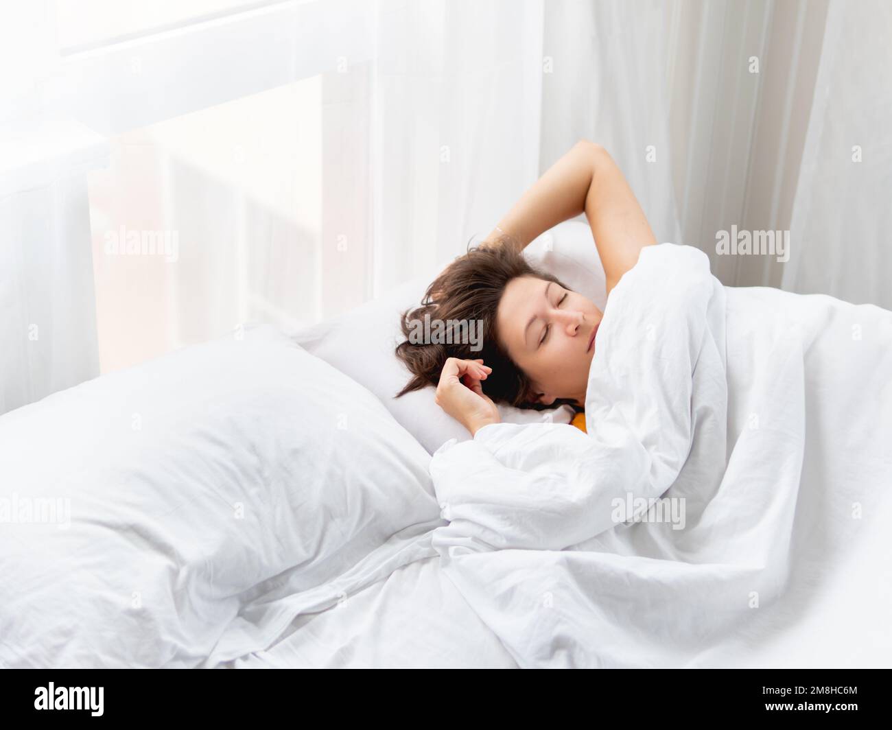 Donna caucasica dorme a letto. Sonno sano sulla biancheria da letto bianca. Mattina a casa accogliente. Foto Stock