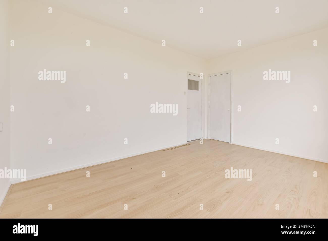 una stanza vuota con pavimenti in legno e pareti bianche, c'è una porta che conduce al lato sinistro della stanza Foto Stock