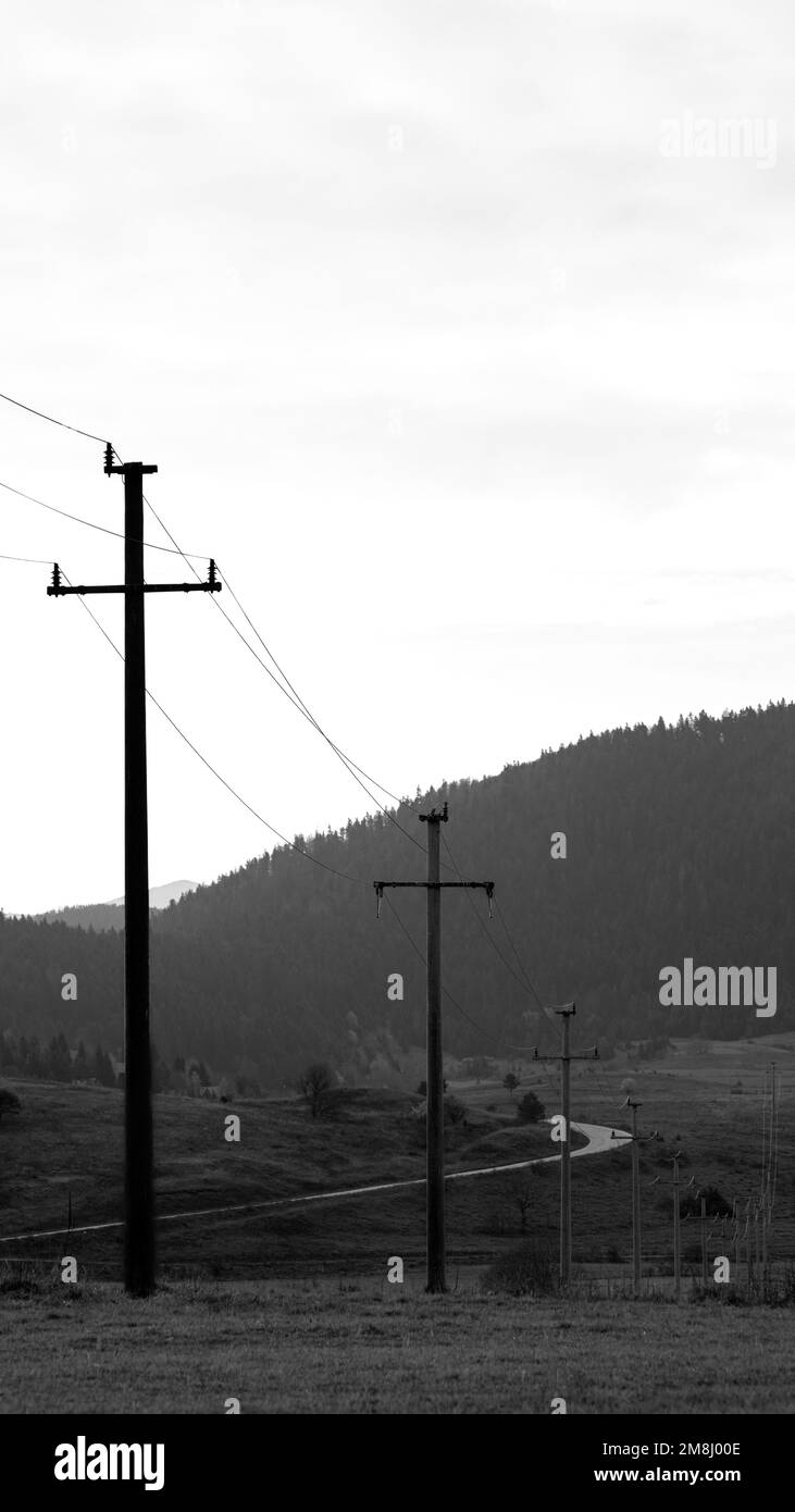 Una scala di grigi di campi con linee elettriche e stazioni intorno, montagne e cielo soleggiato sfondo Foto Stock
