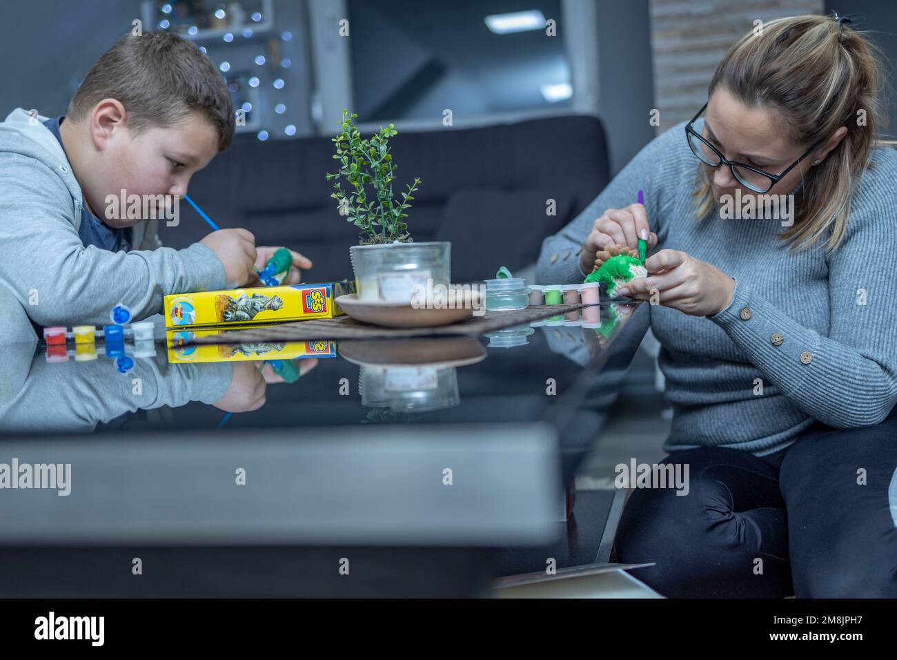 madre e figlio dipingendo figure in ceramica su un tavolo di vetro. entrambi guardare attentamente e dipingere le loro figure.they sono molto focalizzati e precisi Foto Stock