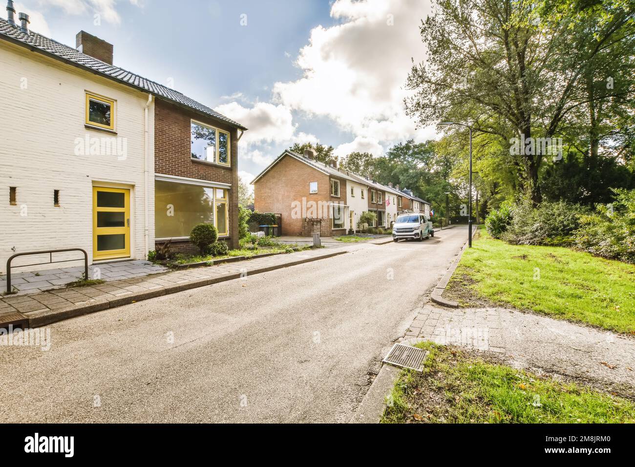 una strada vuota con case sullo sfondo e erba verde su entrambi i lati, c'è una macchina bianca parcheggiata accanto ad essa Foto Stock