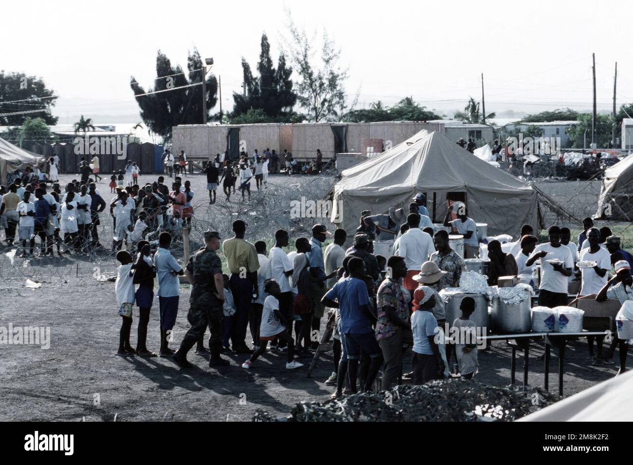 Un poliziotto di sicurezza dell'USAF guarda come i rifugiati haitiani si allinea per la cena all'interno di un campo profughi a Guantánamo Bay, Cuba. Dall'articolo del numero di dicembre 1994 DI AIRMAN Magazine 'Missions Increase Around the World - Ops tempo: Why Am i Here'. Base: Guantánamo Bay Nazione: Cuba (CUB) Foto Stock