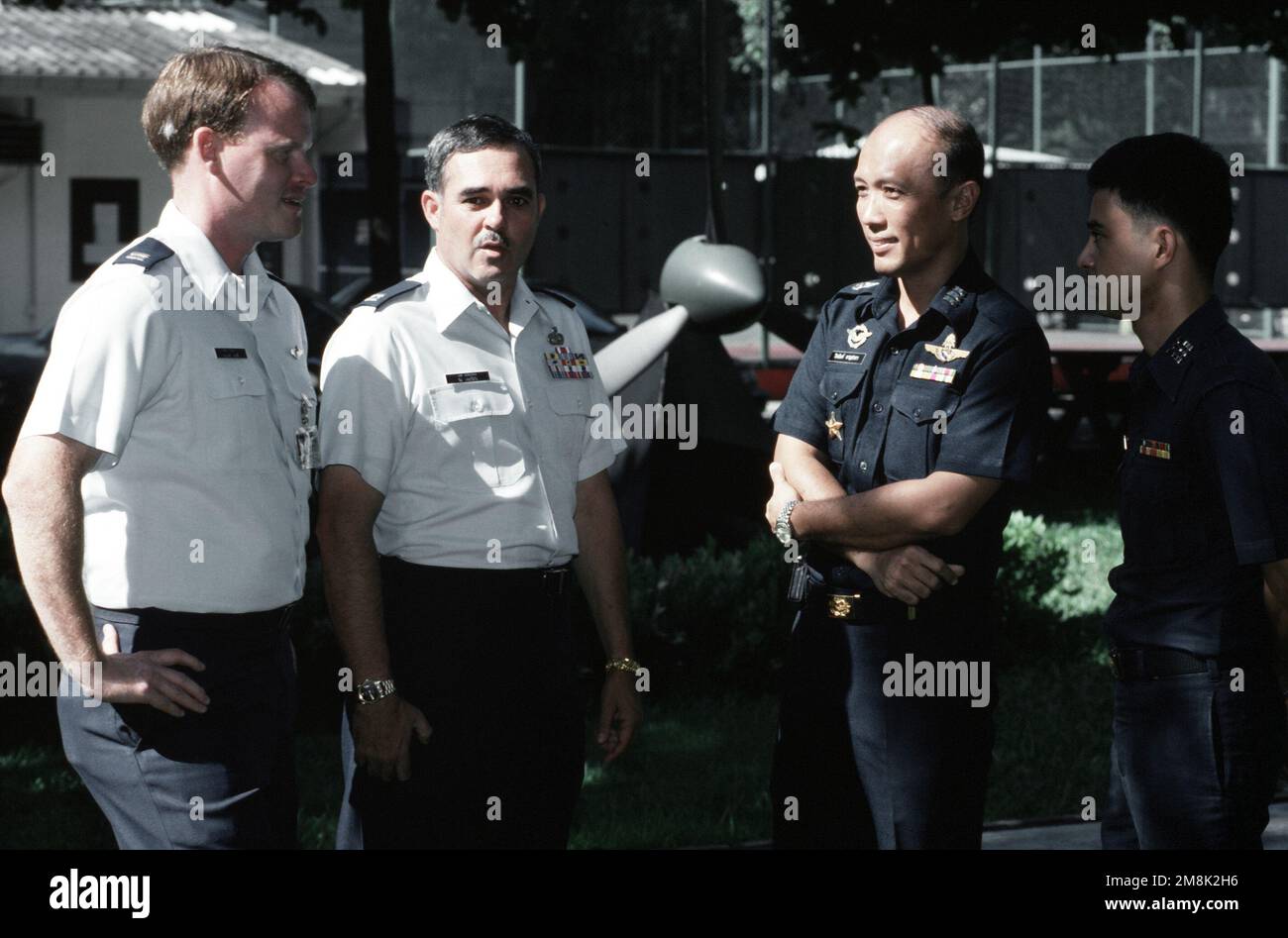 Gli ufficiali dello scambio USAF Capitano Ray Purdy, un istruttore pilota e il Capitano Jim Jernigan chiacchierano con il tenente colonnello Weernan Hansavata, Comandante dello Squadrone 601 della Royal Thai Air Force presso la base aerea Don Muang, Thailandia e il maggiore Panuvat Piumsri, IL CAPO di manutenzione dello squadrone. Dal numero di dicembre 1994 DI AIRMAN Magazine 'vivere in stile thailandese'. Base: Don Muang Air base Paese: Thailandia (THA) Foto Stock