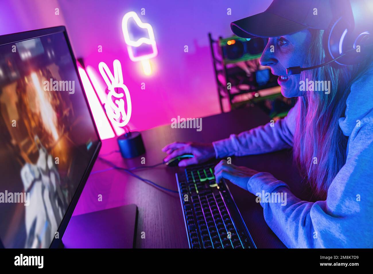 Aggressivo e urlando femmina giocatore giocando in prima persona Sparatutto Online Video Game sul suo potente Personal computer. Camera e PC hanno colorato Neon Foto Stock