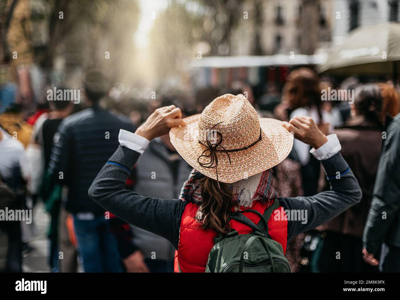 vista posteriore di una donna con cappello e zaino che cammina attraverso un mercato tradizionale in spagna. tiene il cappello. concetto di turismo urbano e vacanze. Foto Stock