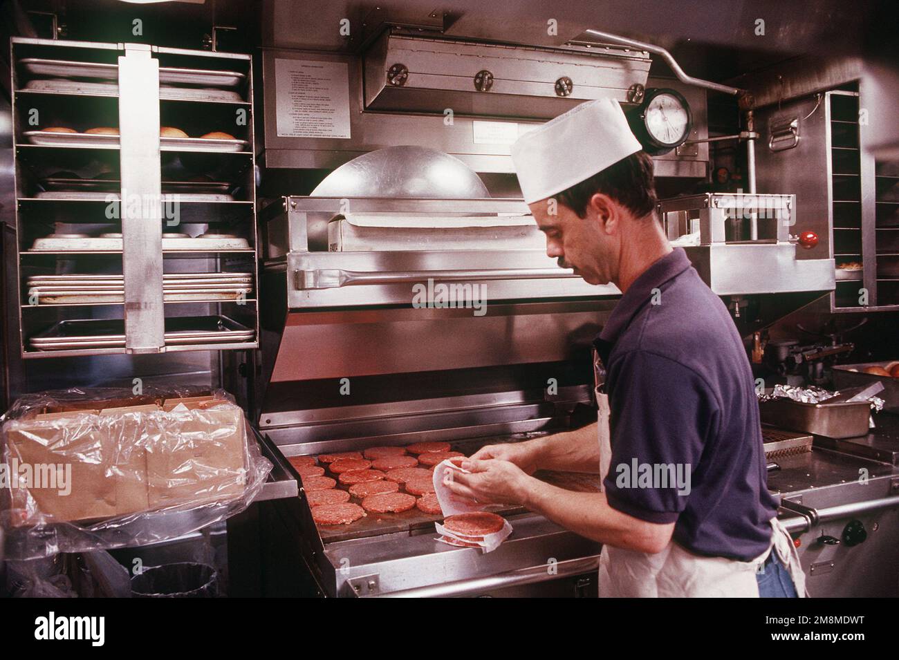 Un cuoco della Marina a bordo del sottomarino di attacco nucleare USS Oklahoma City (SSN-723) prepara hamburger per il pasto a mezzogiorno degli equipaggi. Paese: Mar Mediterraneo (MED) Foto Stock