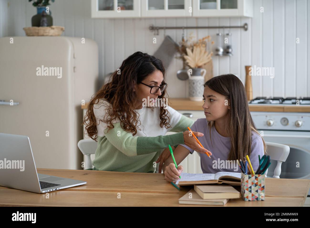 Ragazza confuso adolescente legge libri e fa note nel libro di lavoro della scuola si siede alla scrivania della cucina con la mamma Foto Stock