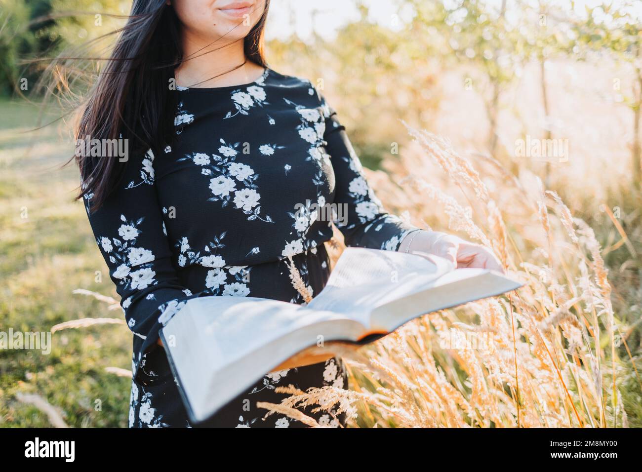 Giovane ragazza cristiana religiosa che tiene e legge la sua bibbia, fuori nel campo al tramonto. Comunione con Dio. Foto Stock