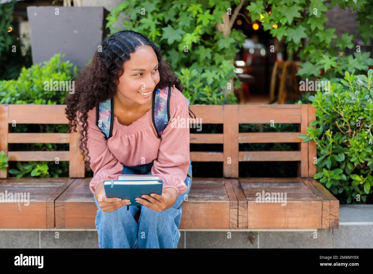 Donna studentesca nera sorridente seduta e in attesa di un compagno di classe fuori dal centro commerciale. Concetto di istruzione Foto Stock