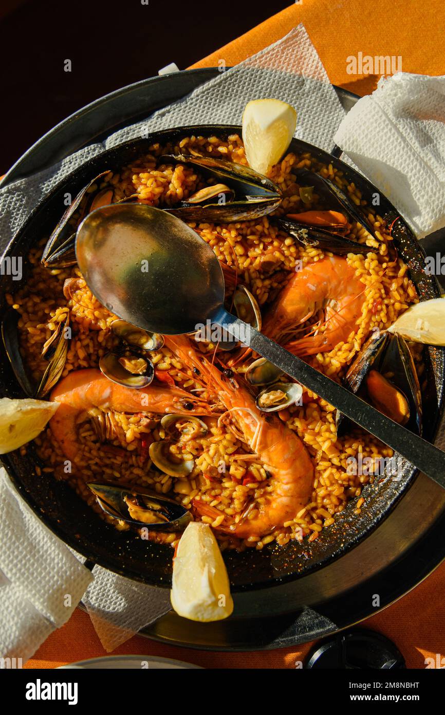 Paella tradizionale servita al ristorante paella di pesce in padella con un  enorme cucchiaio di ferro, gamberi e cozze, limone Foto stock - Alamy