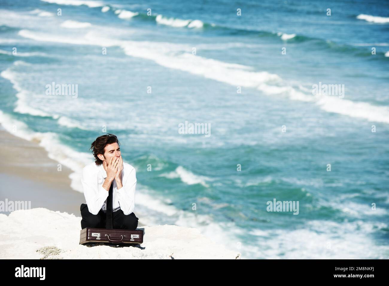 La maestosità della natura. Giovane uomo d'affari seduto su una scogliera sopra l'oceano con la sua valigetta. Foto Stock