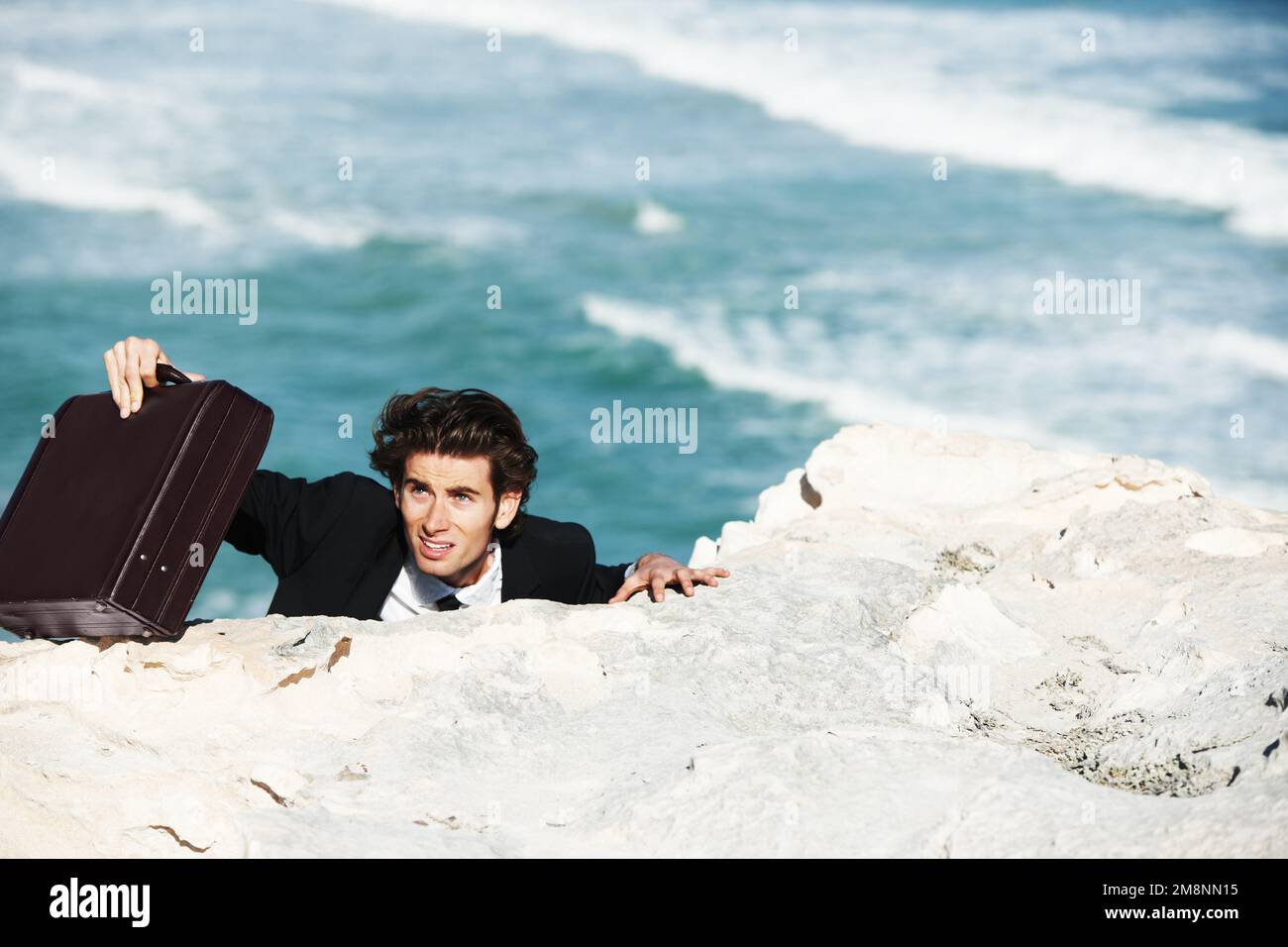 E' una lenta salita al successo. Uomo d'affari che sale sul lato di una scogliera con la sua bramosa con l'oceano sullo sfondo. Foto Stock