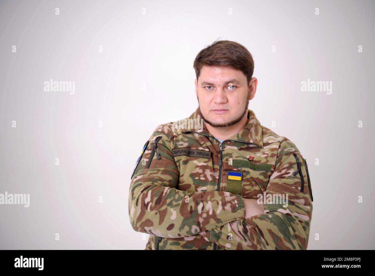 Difensore ucraino. Soldati forze armate dell'Ucraina. Una foto ravvicinata di un uomo militare occhi blu barba maschile mento pulito poppa look badge e bandiera Foto Stock