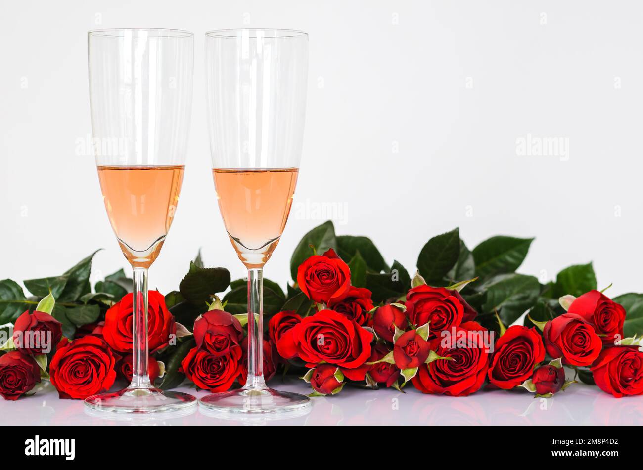 Due bicchieri di vino rosato su sfondo bianco con rose rosse per la cucina di San Valentino. Foto Stock