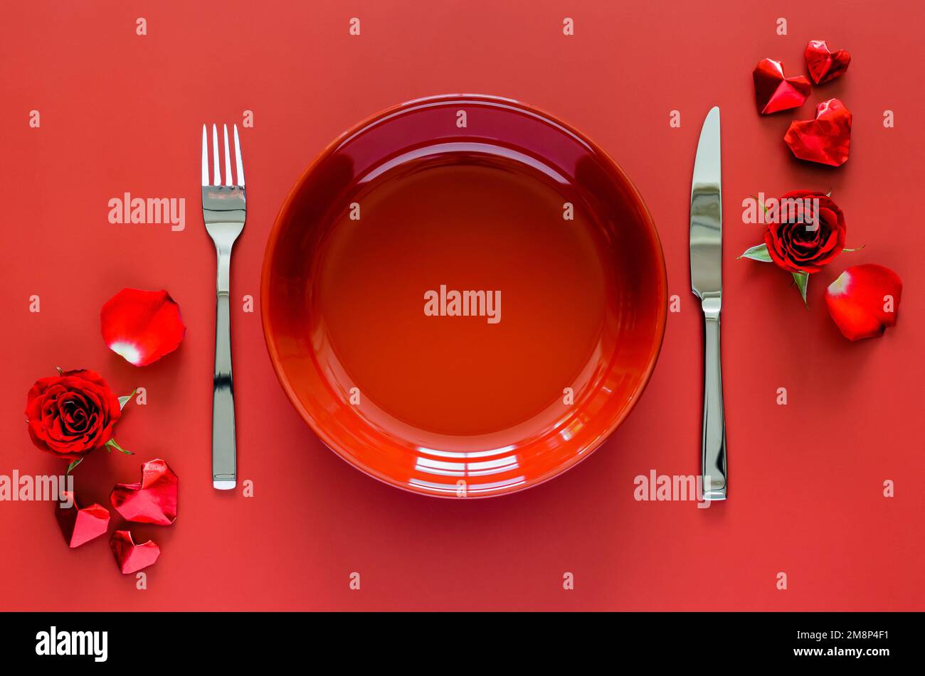 Concetto di ristorazione di San Valentino con piatto rosso, forchetta e coltello messi su tavolo rosso con rosa e amore piega di carta. Foto Stock