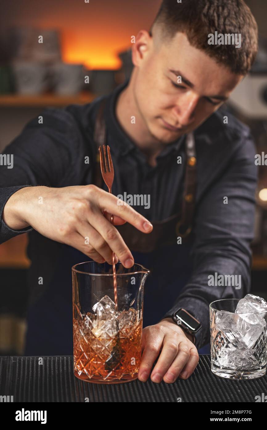 Giovane barman che mescola cocktail alcolico fresco con sciroppi di frutta dolce al banco del bar Foto Stock