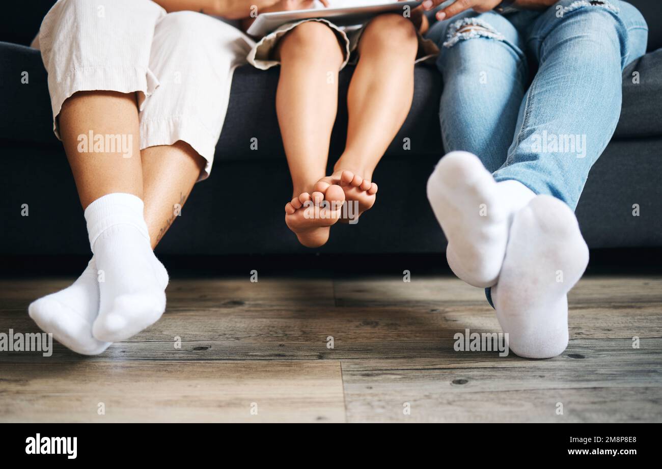 Primo piano di una famiglia seduta su un divano utilizzando un tablet nel salotto di casa. I piedi della famiglia si rilassano mentre si siede su un divano durante il giorno Foto Stock