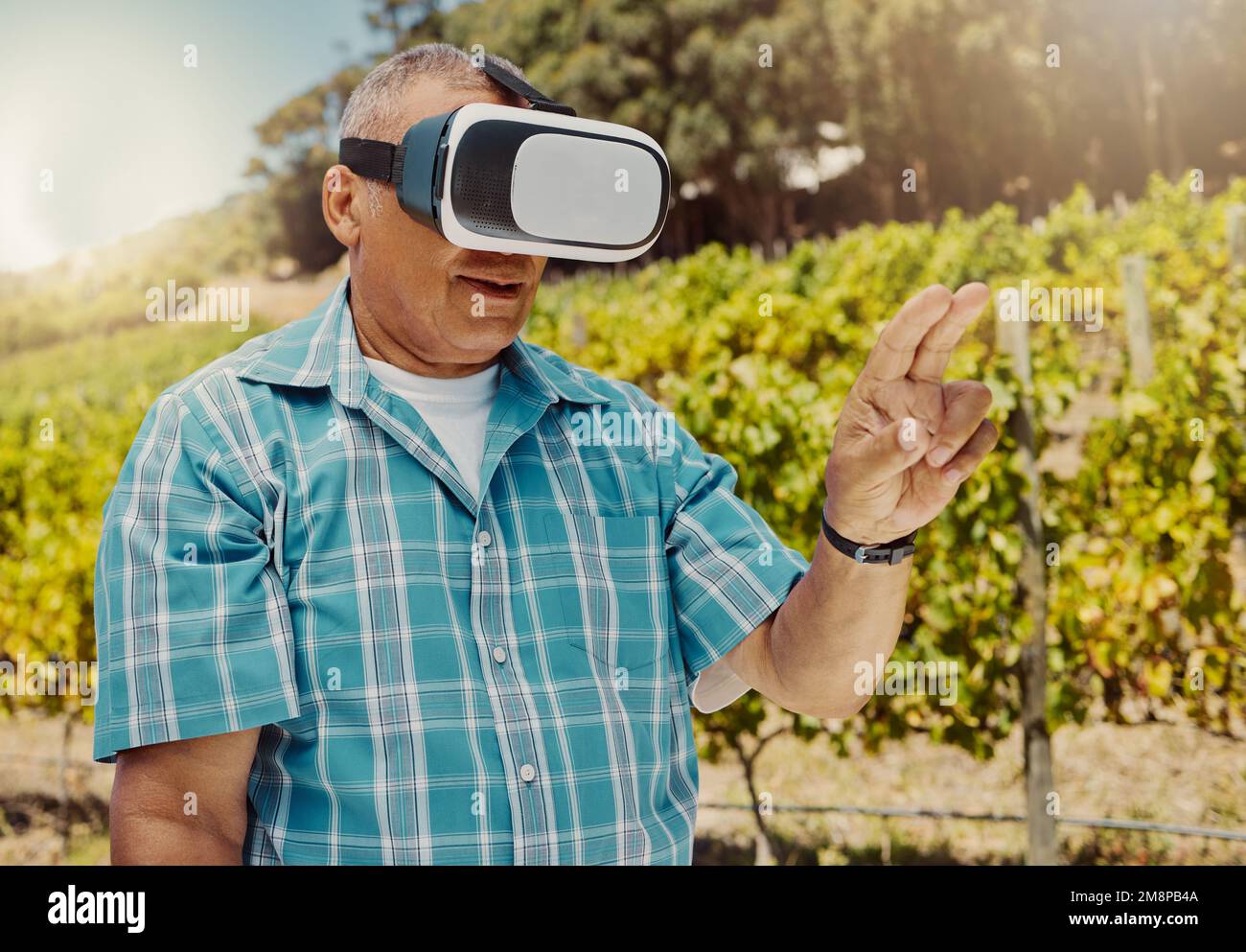 Un agricoltore senior misto che utilizza un visore per la realtà virtuale attraverso il metaverse. Uomo anziano ispanico che tocca la realtà aumentata in multiverso. Vecchio Foto Stock