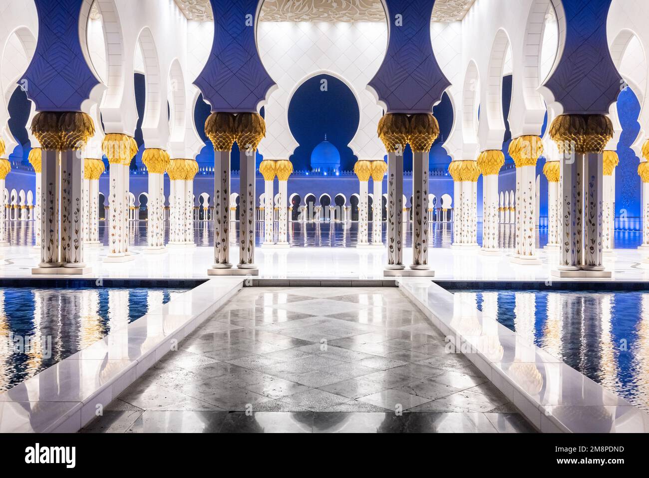foto notturna simmetrica del colonnato della moschea dello sceicco Zhayed, con una passerella in marmo circondata dall'acqua Foto Stock