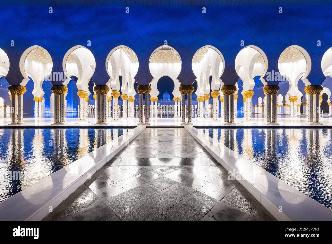foto notturna simmetrica del colonnato della moschea dello sceicco Zhayed, con una passerella in marmo circondata dall'acqua Foto Stock