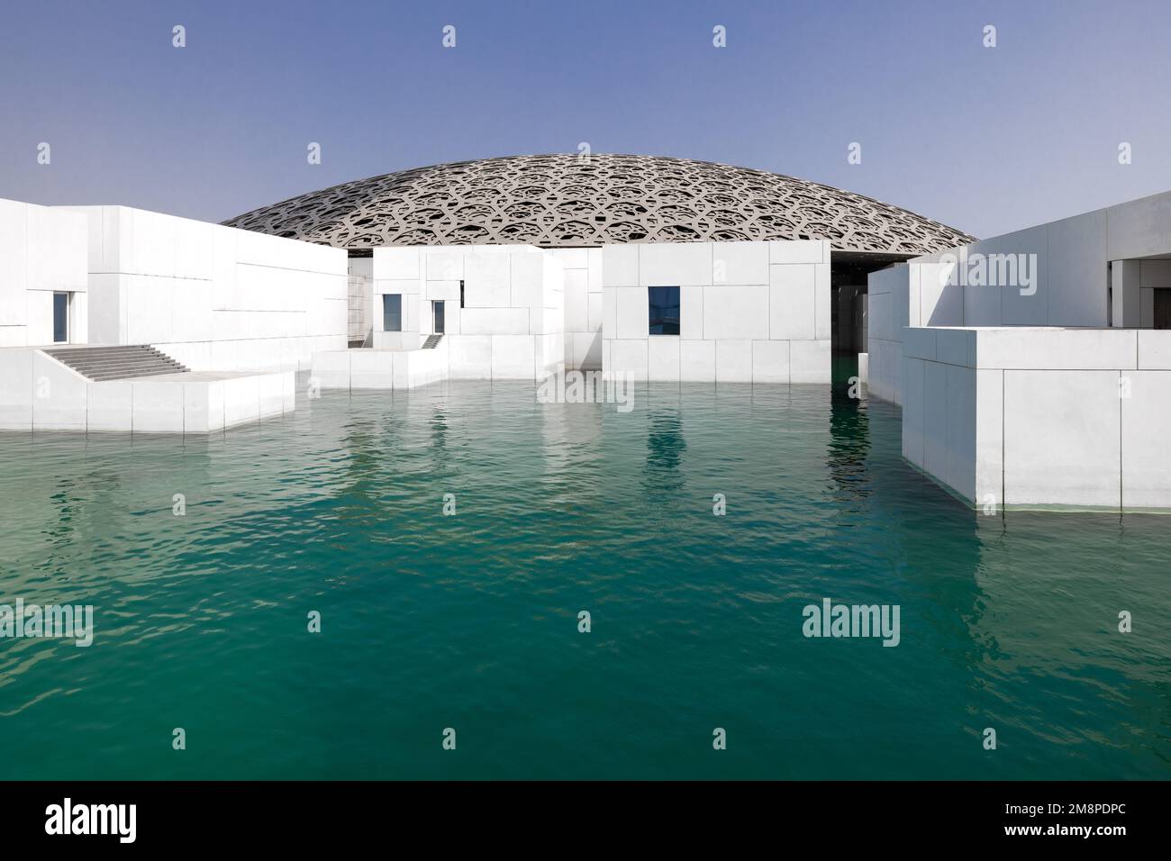 L'esterno del moderno edificio del Louvre ad Abu Dhabi, con la cupola a graticcio e le pareti in marmo bianco, circondate dall'acqua Foto Stock