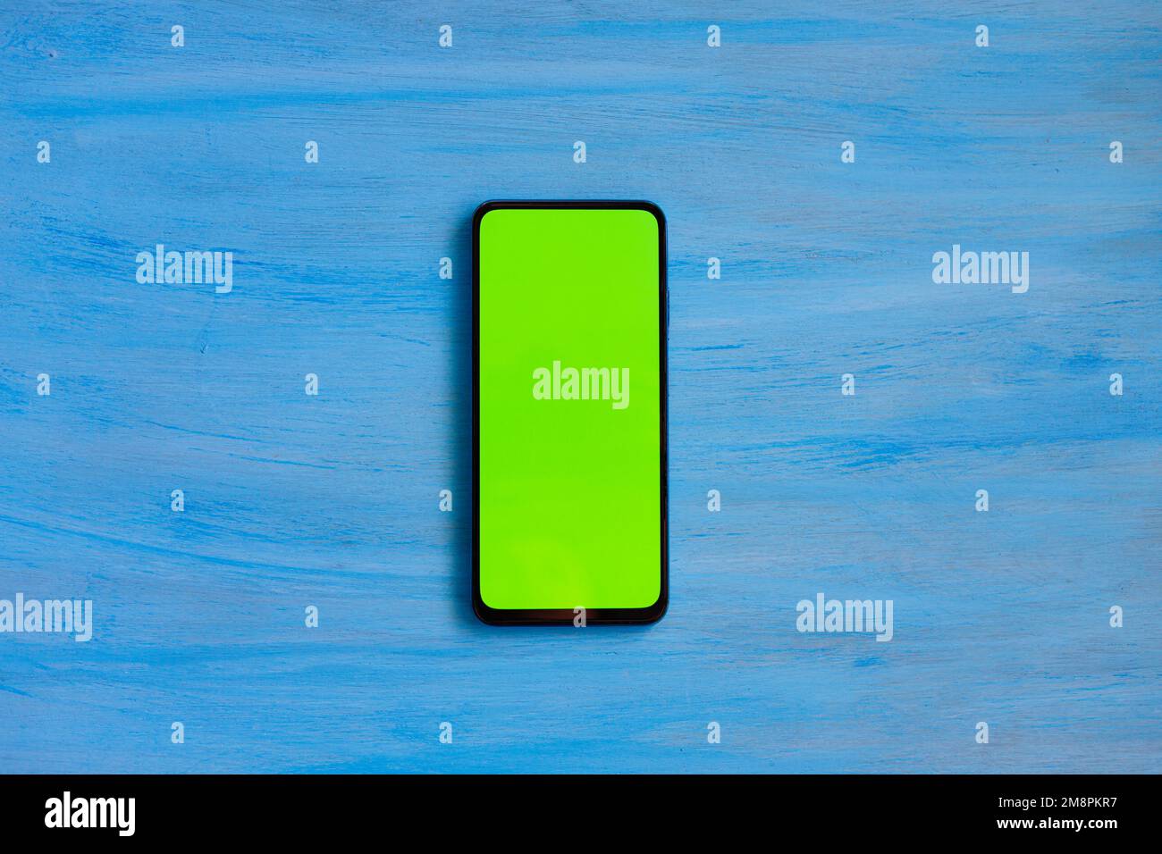 Telefono smartphone, schermo verde su sfondo blu legno vista dall'alto. Foto Stock