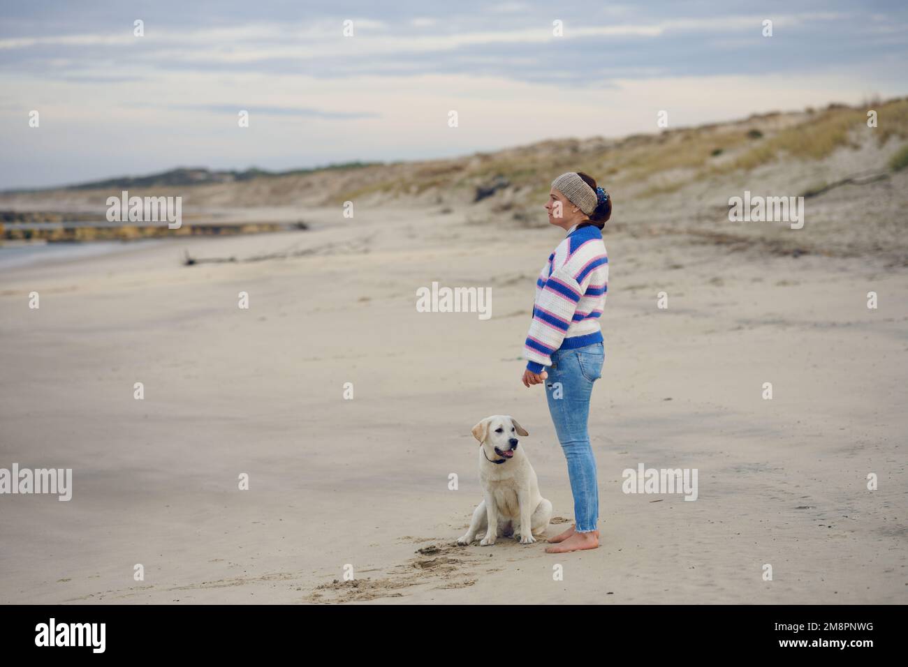 Donna brunetta di mezza età sulla spiaggia vuota con il suo cane labrador Retriever Foto Stock