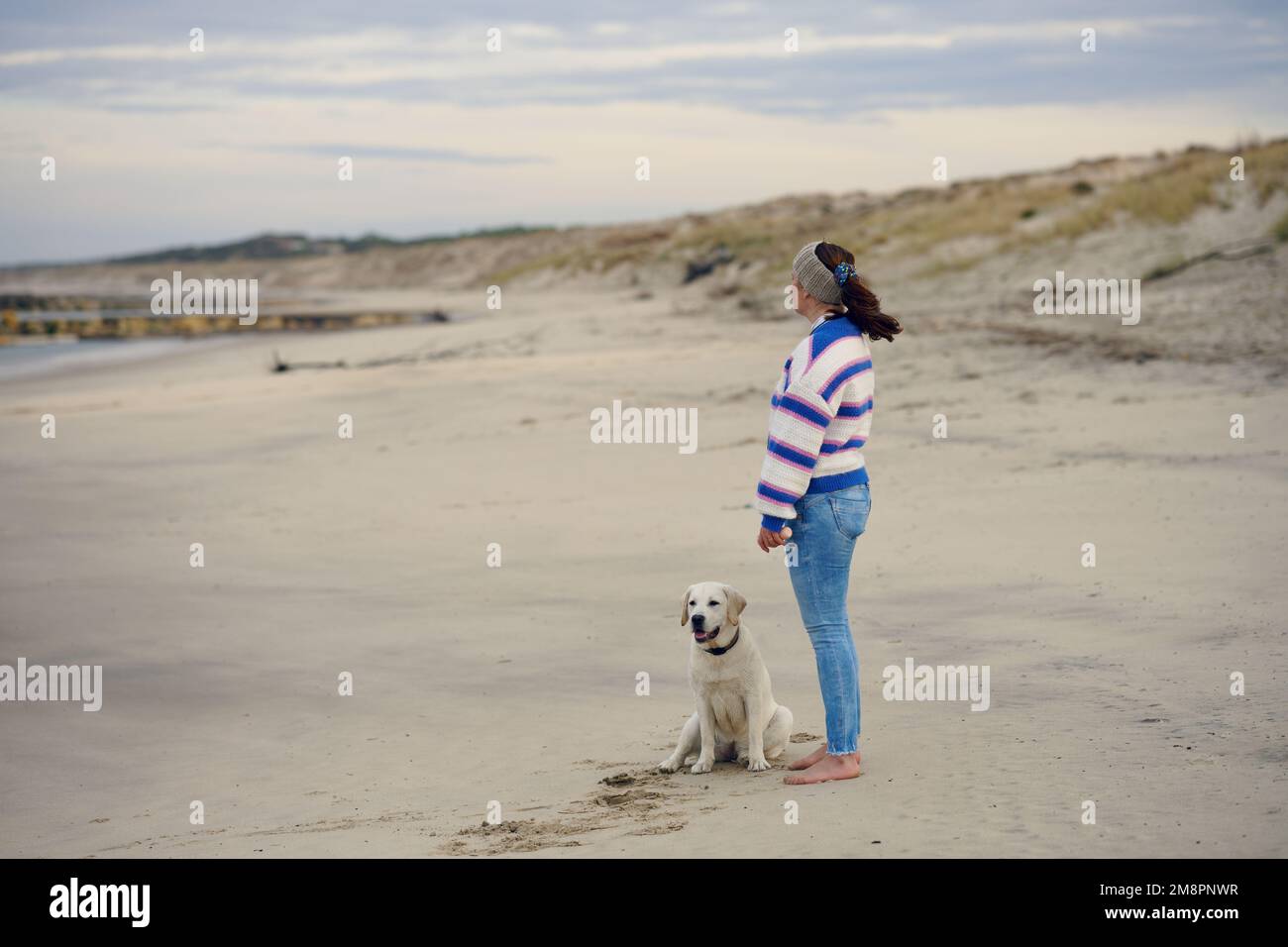 Donna brunetta di mezza età sulla spiaggia vuota con il suo cane labrador Retriever Foto Stock