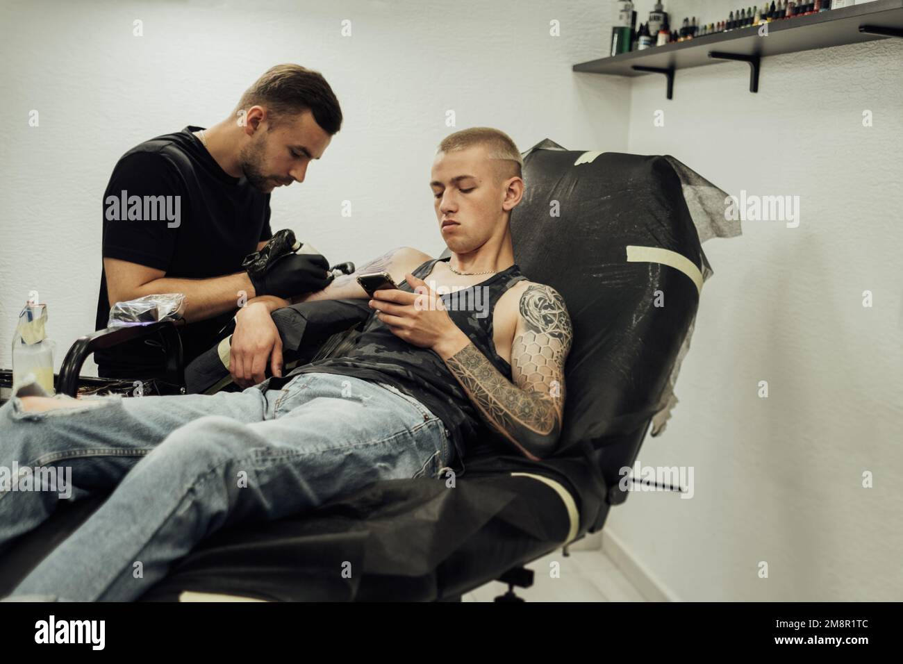 Uomo tatuato sul processo di creazione di nuovo tatuaggio a Studio, artista maschile disegna sulla pelle del cliente Foto Stock