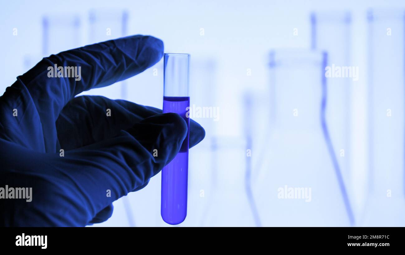 attrezzature di laboratorio. Provetta. Fiala con liquido blu. Una mano in un guanto medico è in attesa di una provetta. Laboratorio. Foto Stock