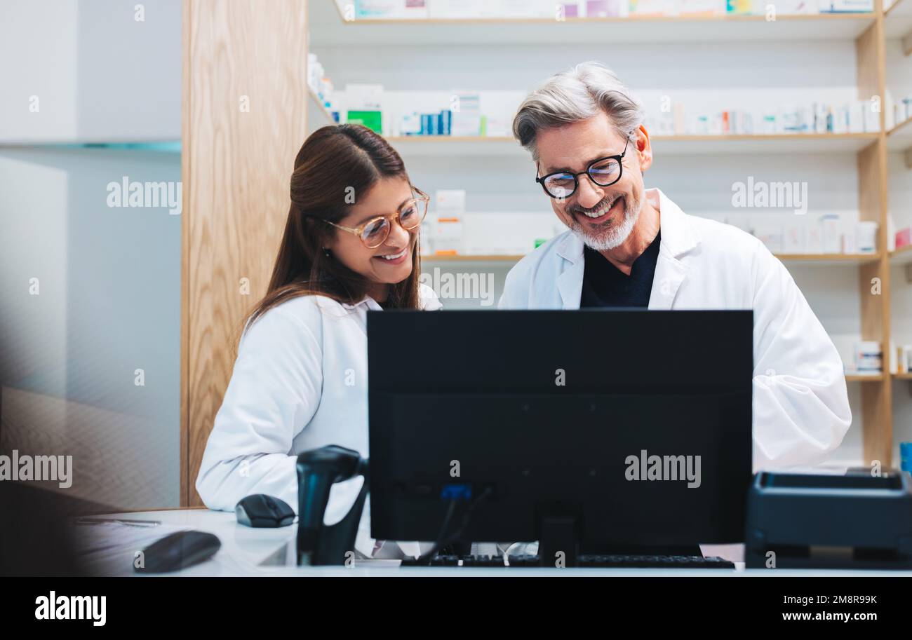 I farmacisti felici videochiamano un paziente su un computer in un chimico. Fornitori di servizi sanitari maturi che elaborano prescrizioni online in farmacia. Foto Stock