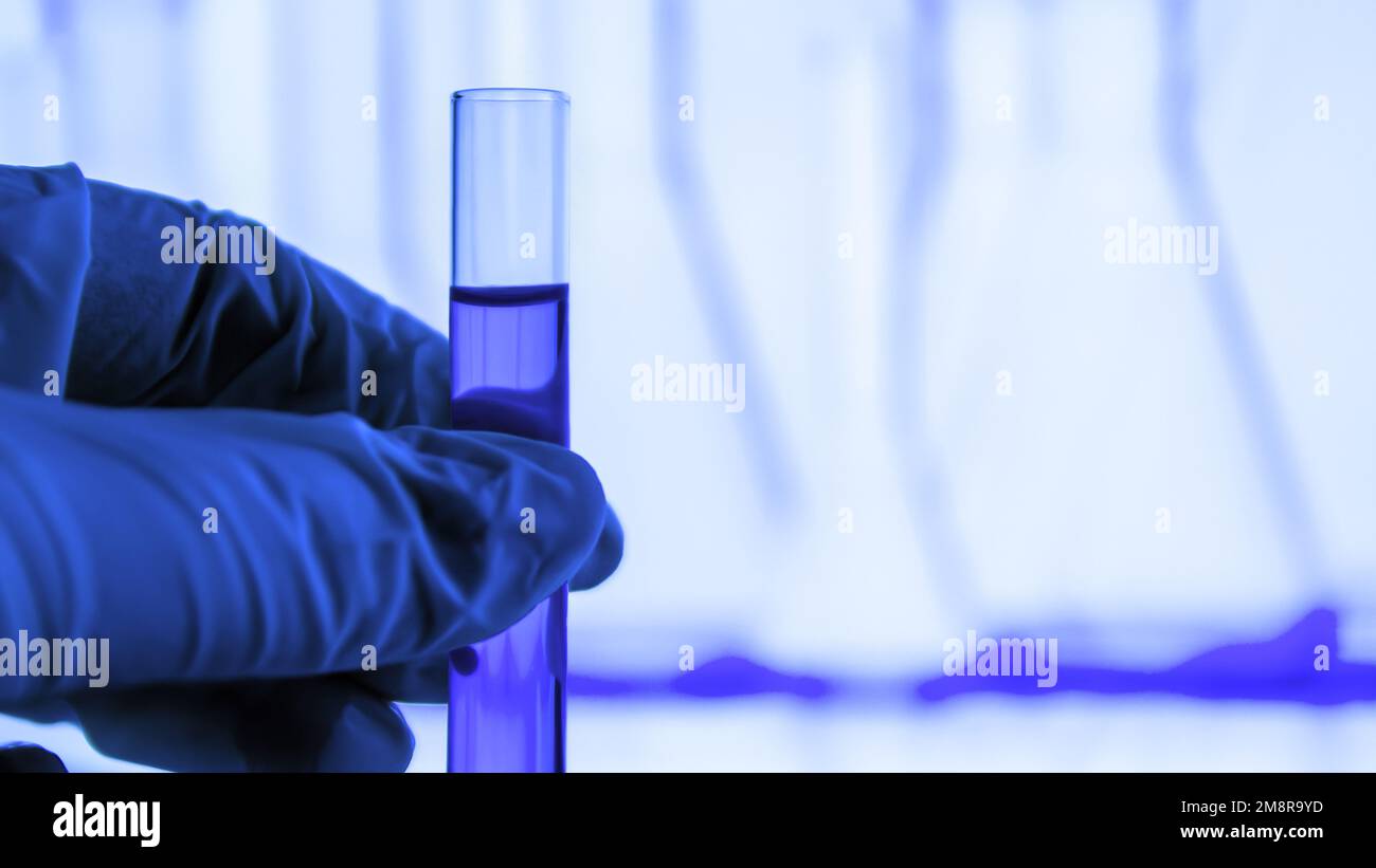 attrezzature di laboratorio. Provetta. Fiala con liquido blu. Una mano in un guanto medico è in attesa di una provetta. Laboratorio. Foto Stock