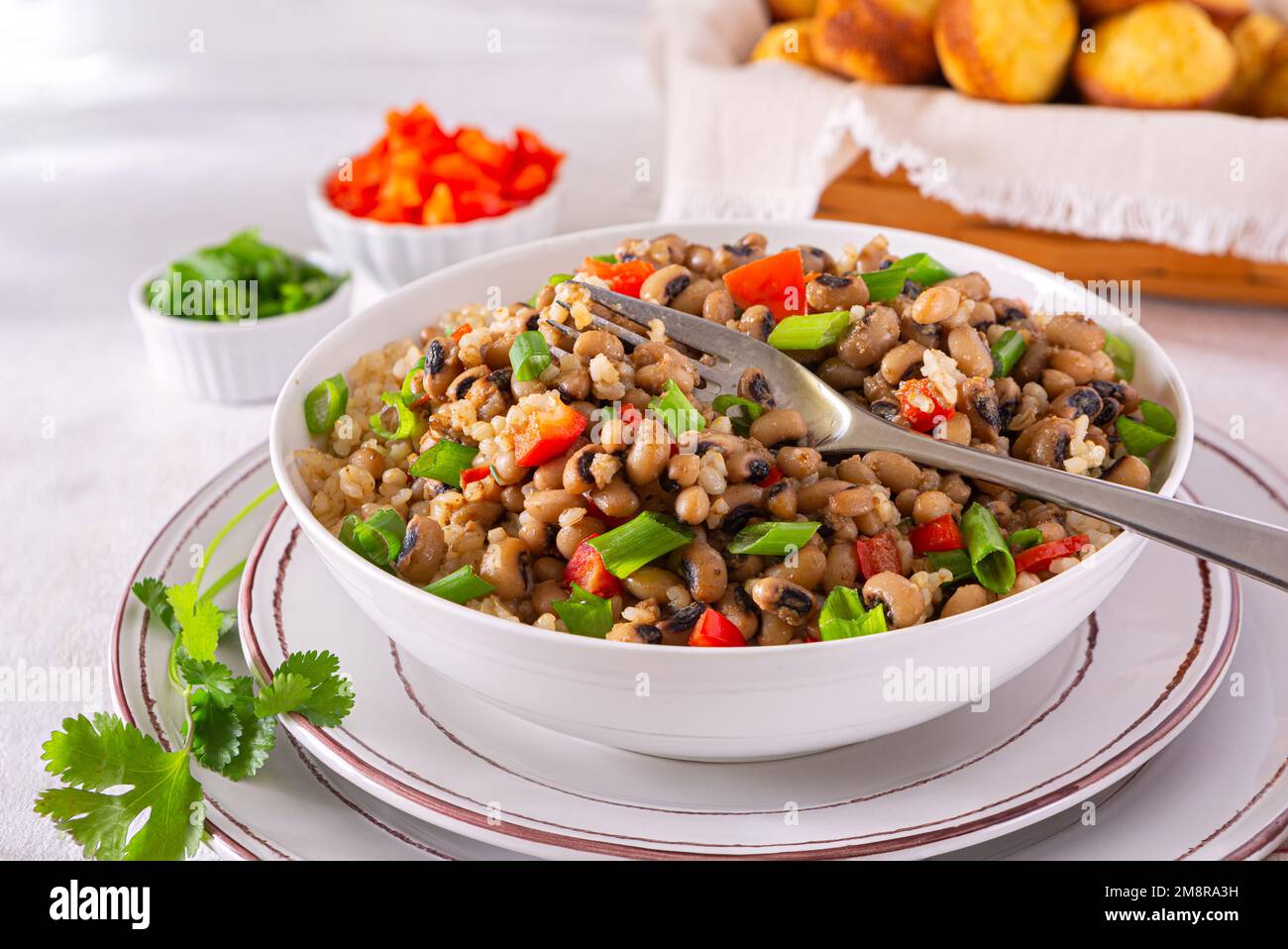 Versione a base di piante del piatto meridionale americano hoppin John fatto con piselli dell'occhio nero, riso marrone, cipolla verde, peperone rosso e muffin al pane di mais nel b Foto Stock