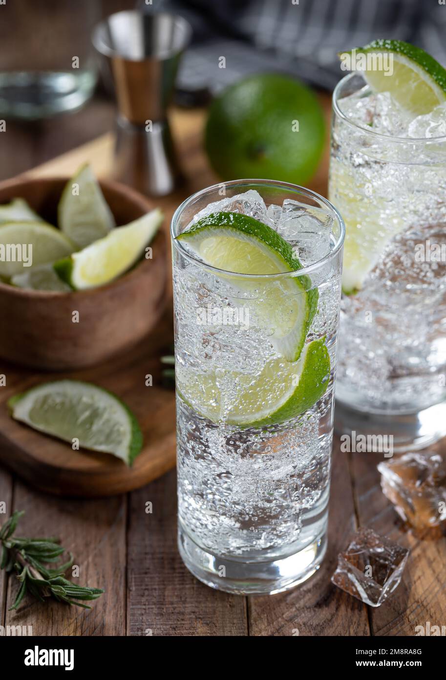 Cocktail tonico e gin con fettine di lime e ghiaccio su un tavolo rustico in legno Foto Stock