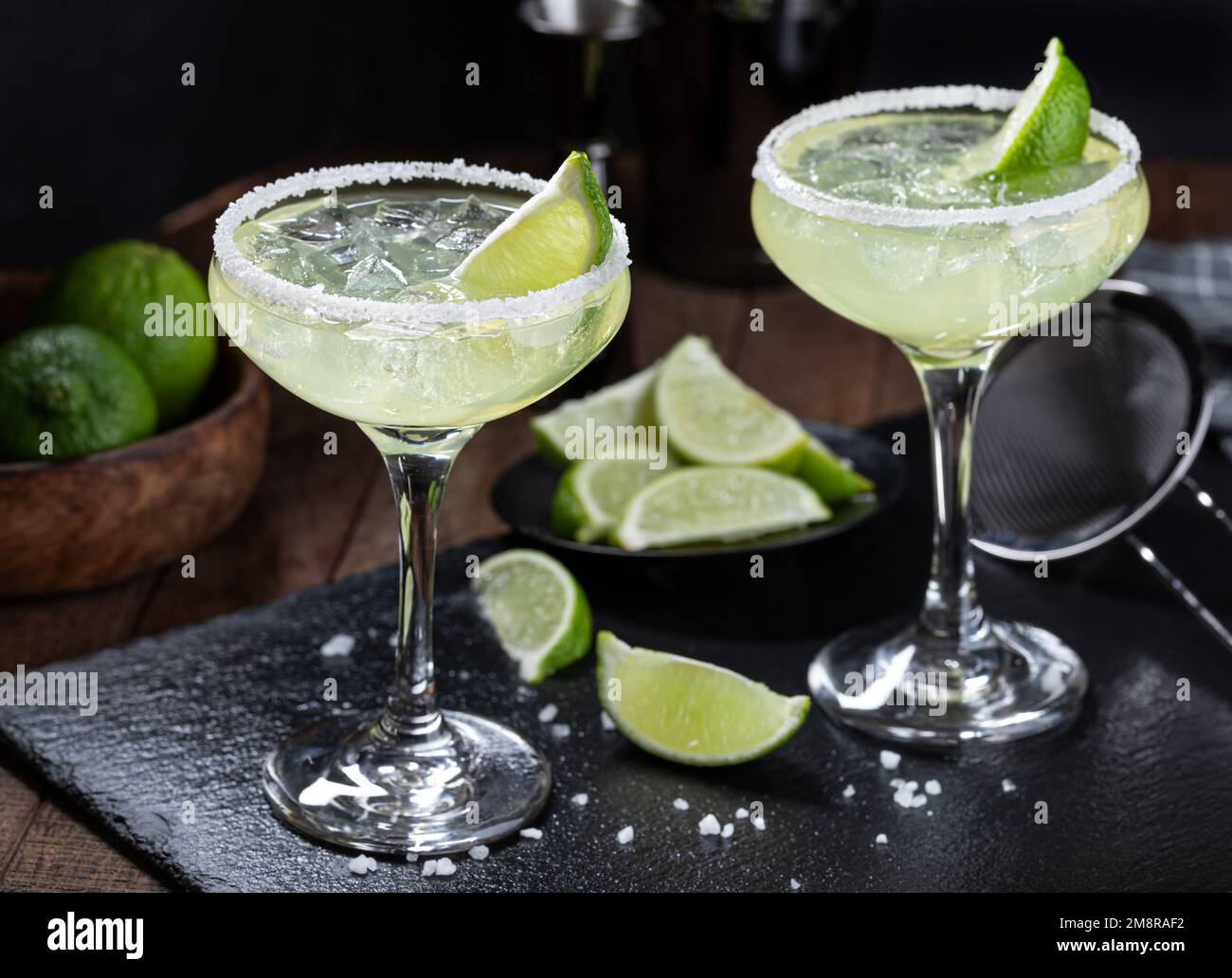 Cocktail Margarita con bordo di ghiaccio, lime e sale su una tavola di ardesia nera Foto Stock