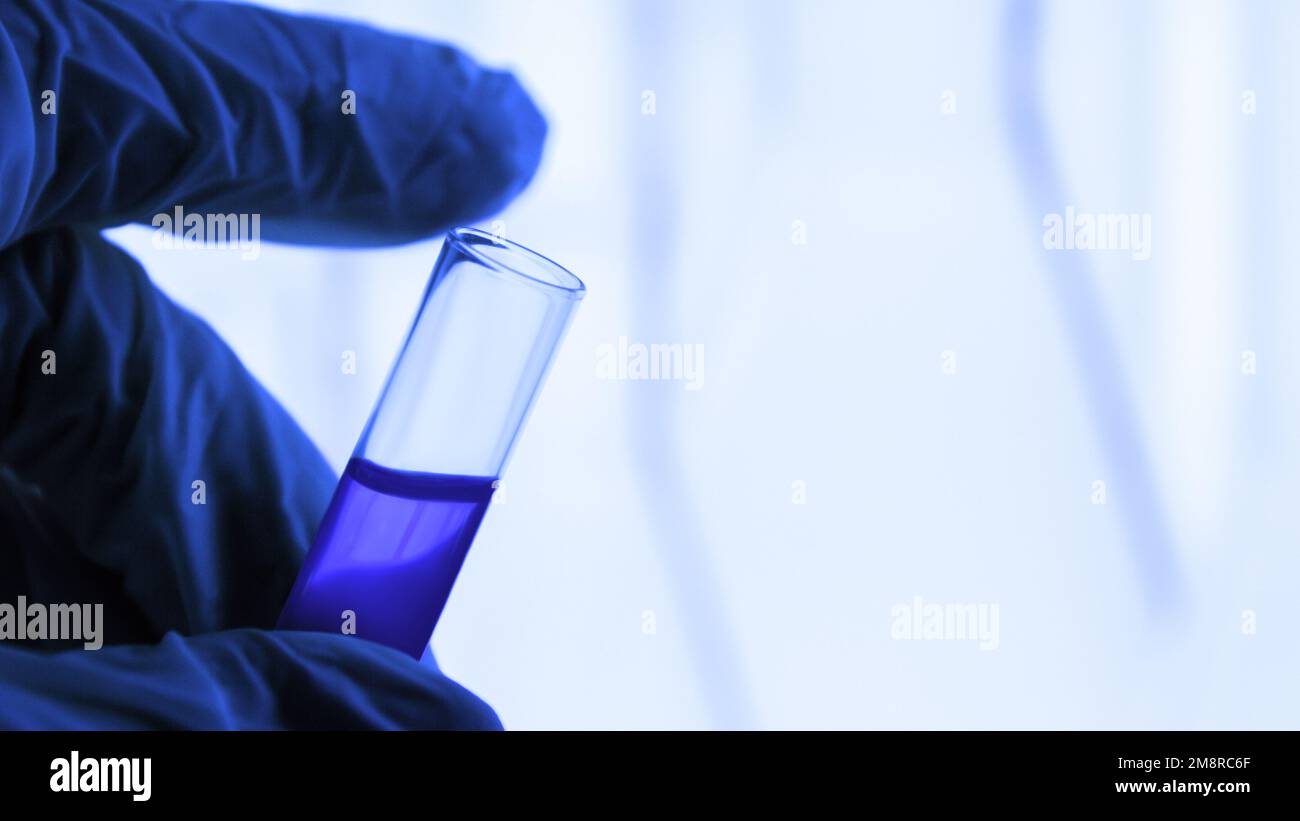 attrezzature di laboratorio. Provetta. Fiala con liquido blu. Una mano in un guanto medico è in attesa di una provetta. Laboratorio. Foto Stock