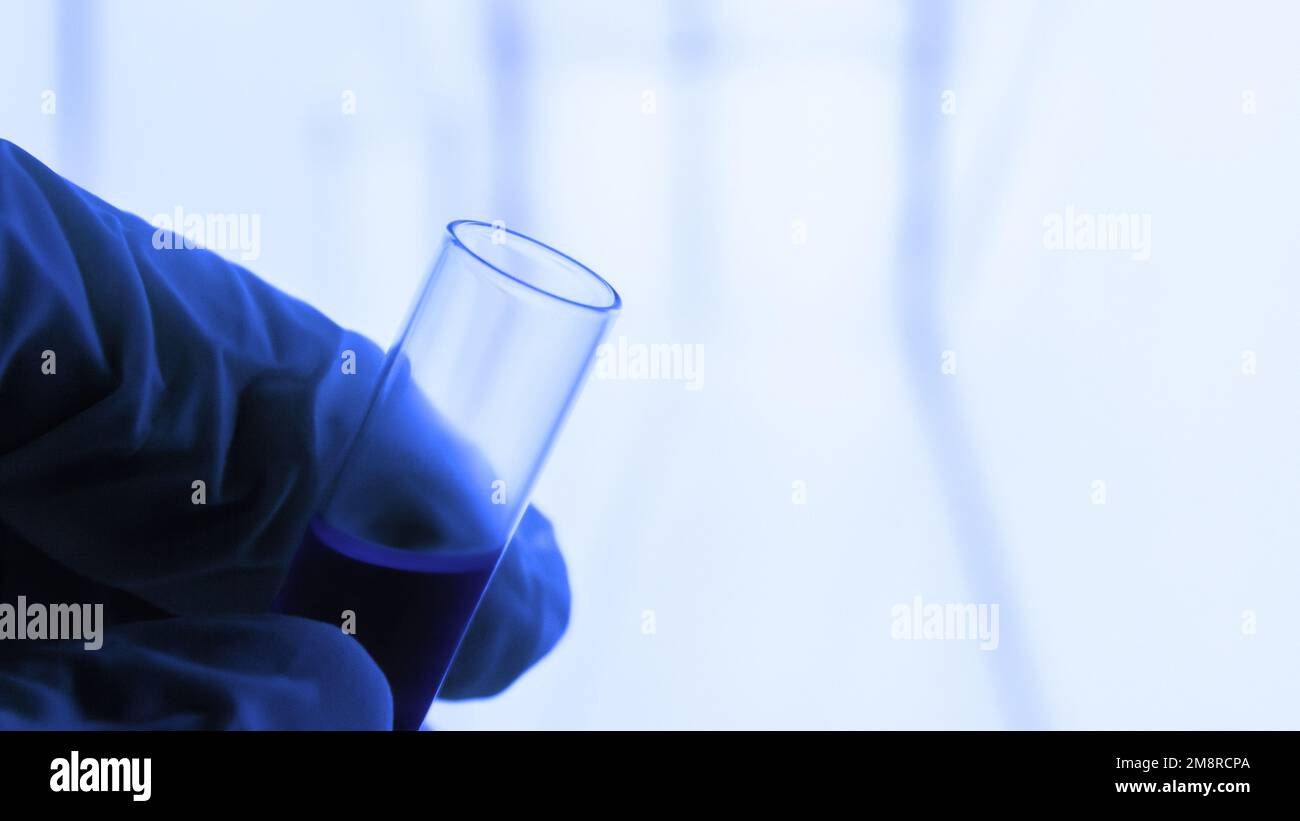 attrezzature di laboratorio. Provetta. Fiala con liquido blu. Una mano in un guanto medico è in attesa di una provetta. Laboratorio. Foto Stock
