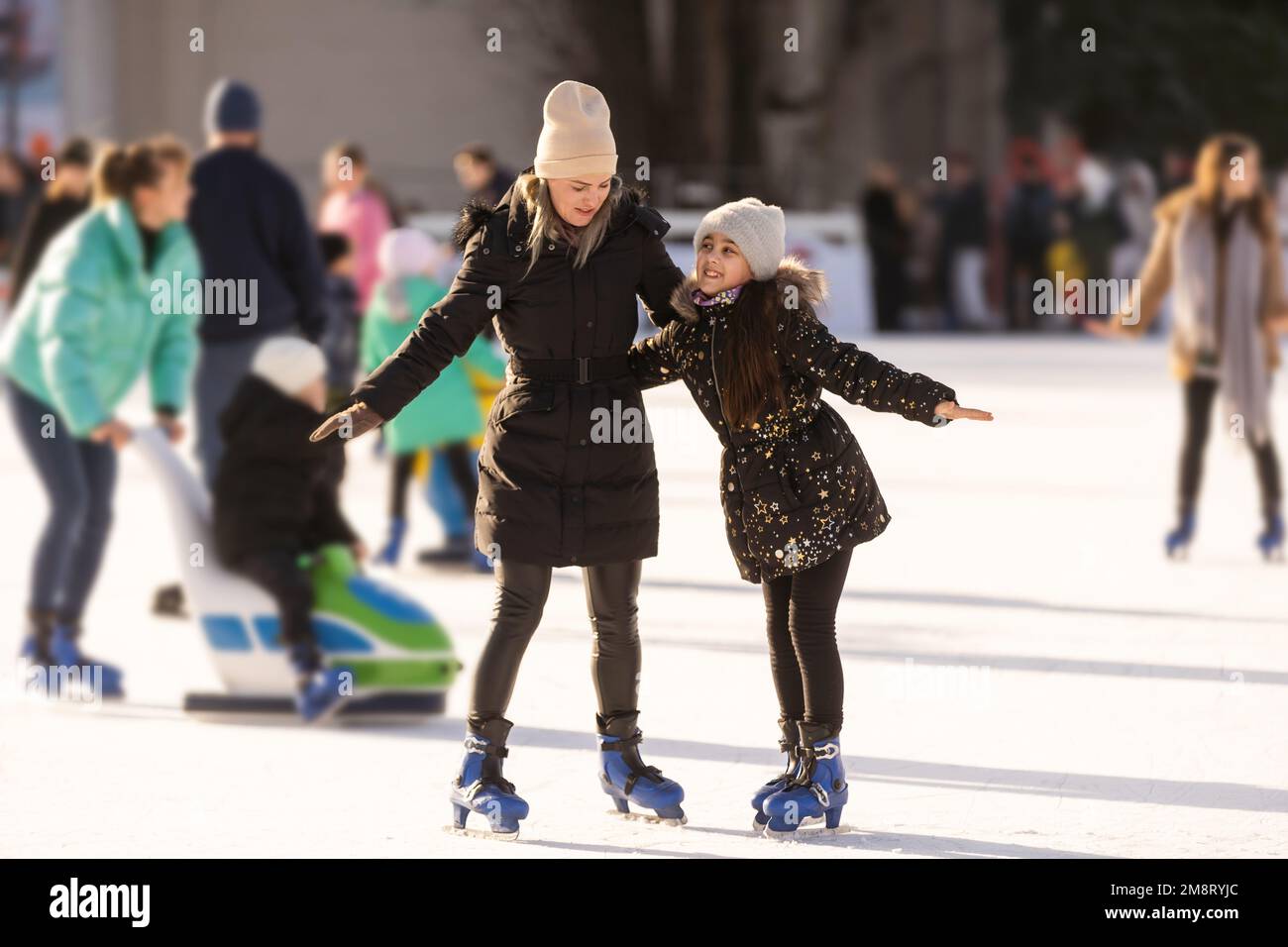 Azione scatto di bella donna che insegna a sua figlia come pattinare su ghiaccio Foto Stock