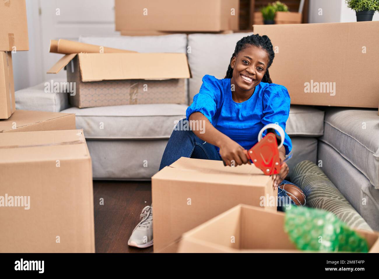 Donna afroamericana sorridente sicuro imballaggio scatola di cartone in nuova casa Foto Stock