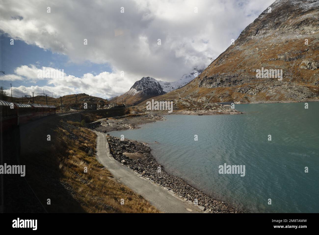 Treno Bernina Express che corre lungo il lago di montagna sulle Alpi, in Svizzera Foto Stock