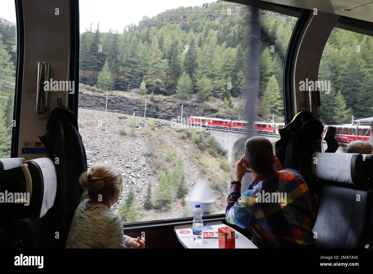 Vista dall'interno del Bernina Express mentre il treno naviga su una curva che sale sulla montagna, sulle Alpi, sulla Svizzera Foto Stock