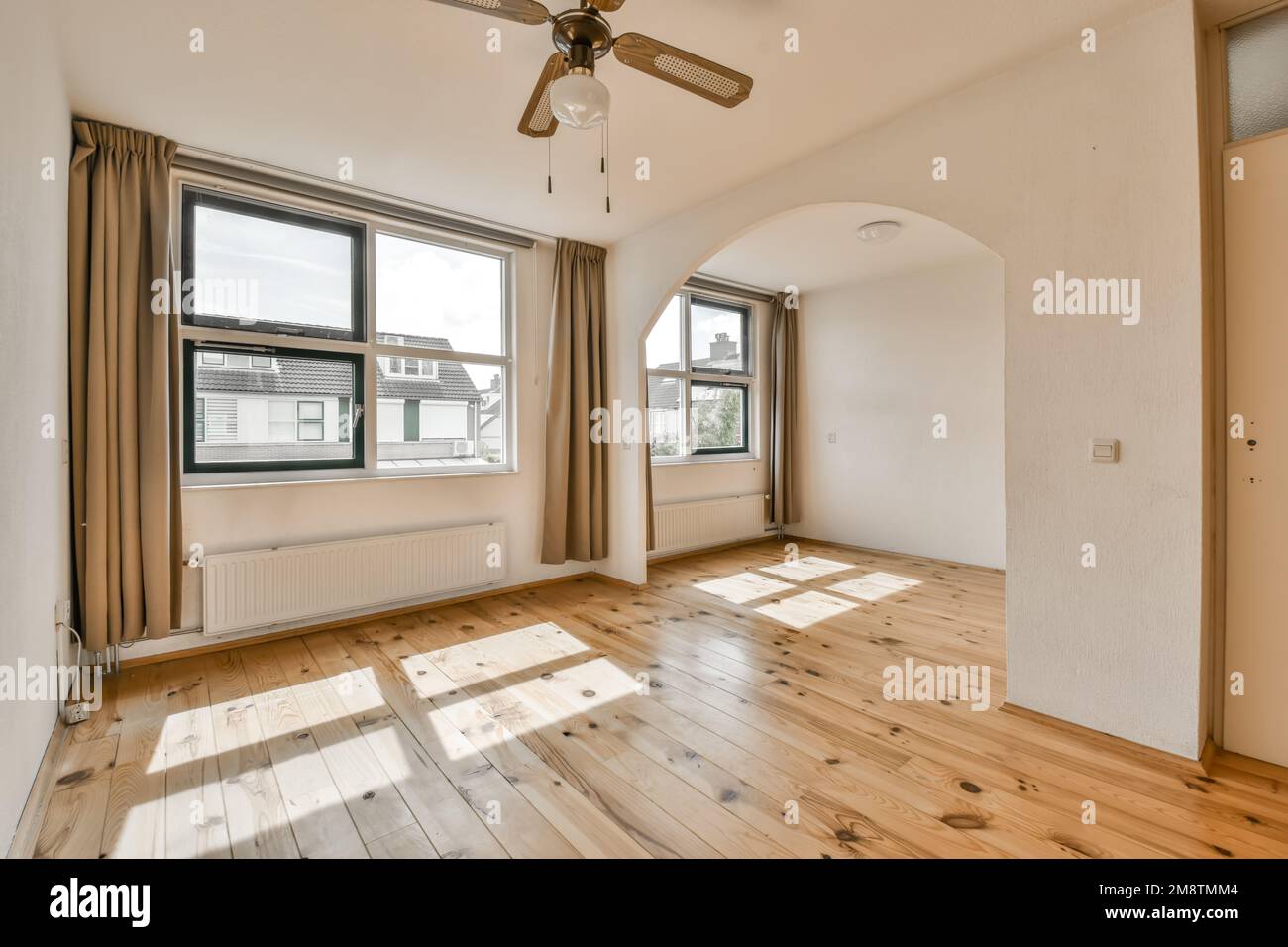 un soggiorno vuoto con pavimento in legno e ventilatore a soffitto nel centro della stanza è molto grandi finestre Foto Stock