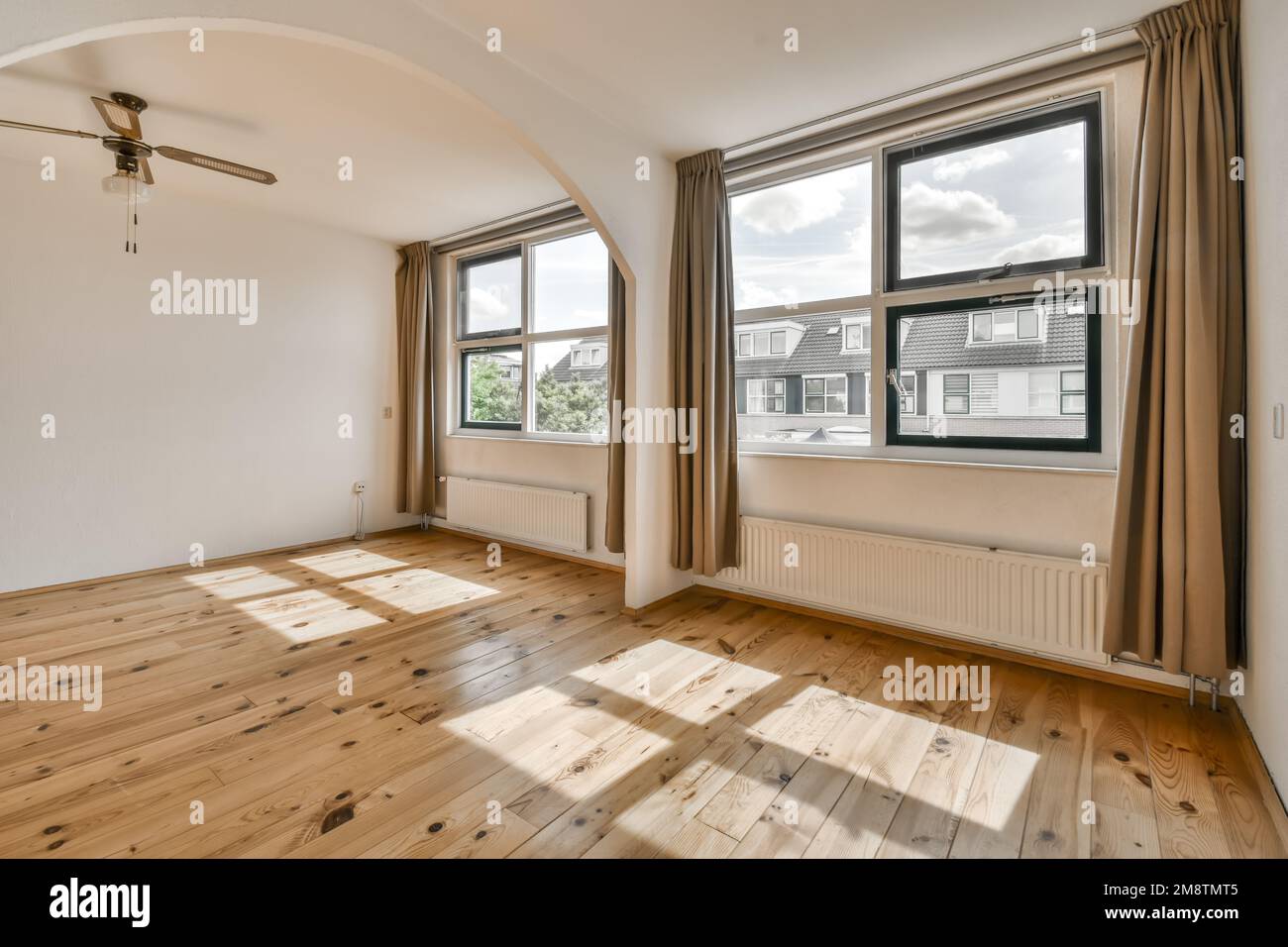 un soggiorno vuoto con pavimento in legno e grandi finestre che si affacciano sulla strada di fronte alla casa Foto Stock