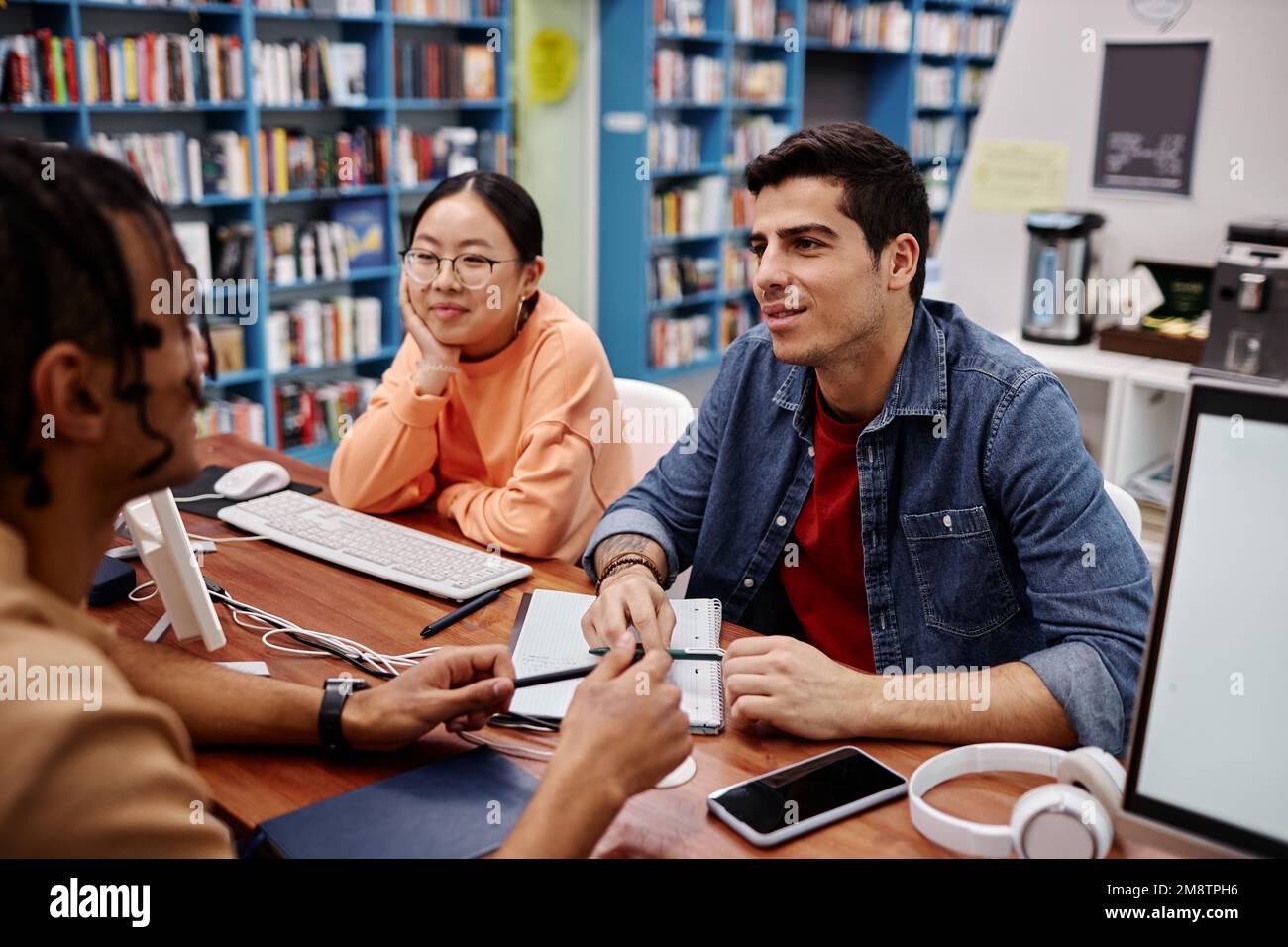 Gruppo multietnico di giovani che studiano insieme nella biblioteca universitaria e discutono dei compiti a casa Foto Stock