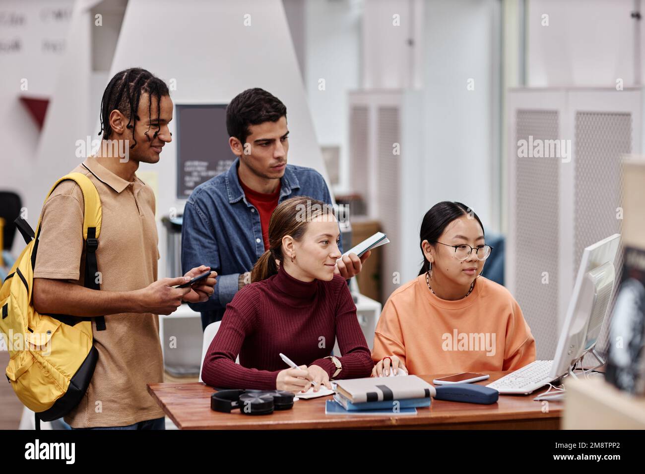 Gruppo multietnico di giovani che studiano in biblioteca universitaria e utilizzano il computer insieme Foto Stock