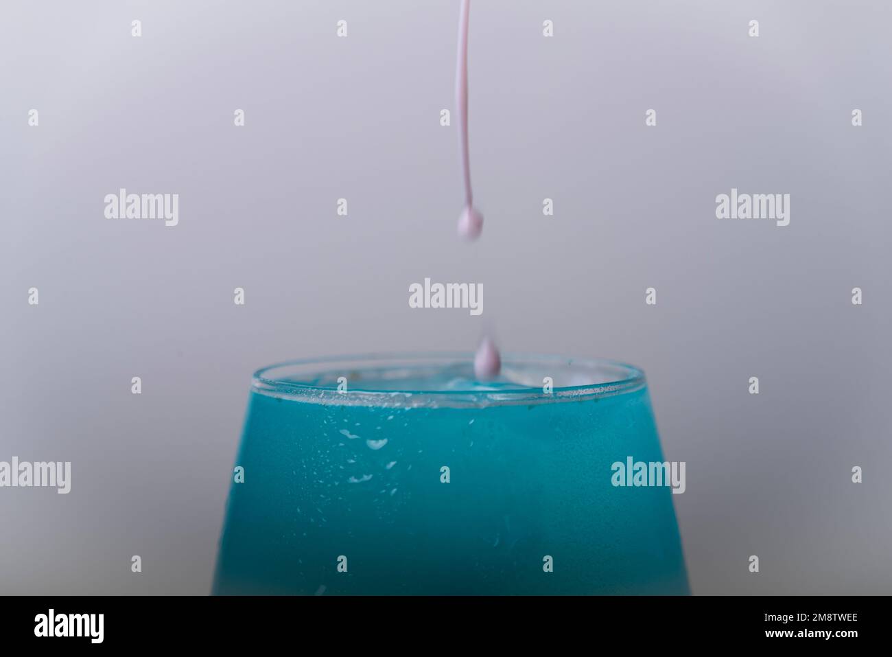 Le gocce di colore cadono sul bicchiere di vino con il liquido di colore chiaro Foto Stock