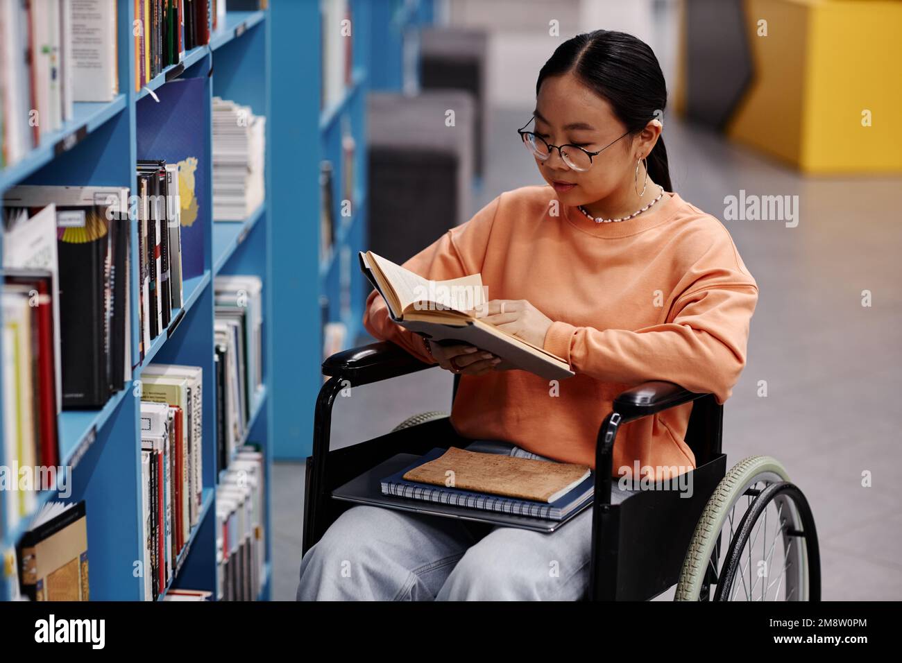 Alto angolo ritratto di ragazza asiatica con disabilità in biblioteca università impostazione lettura libri Foto Stock