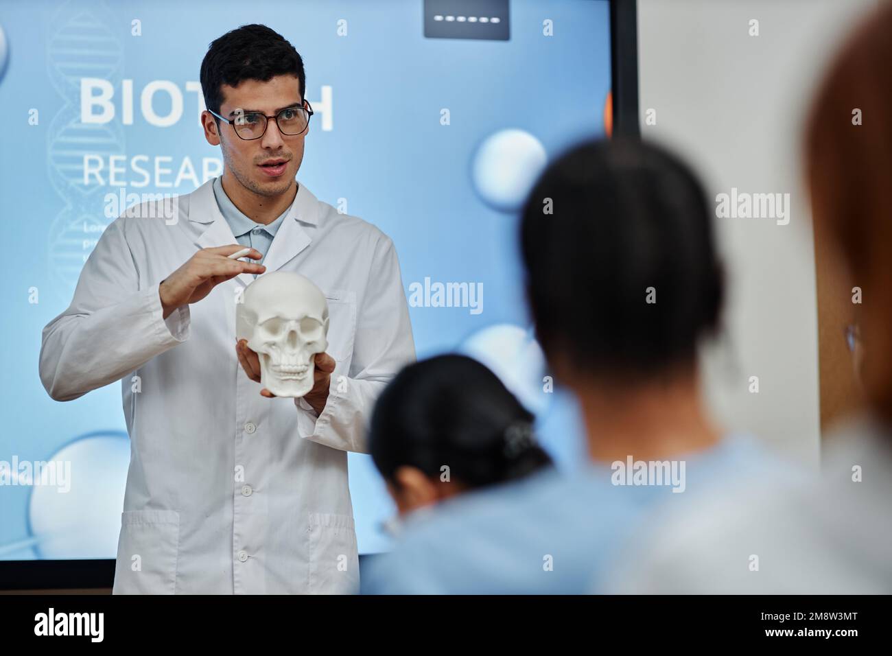 Vita in su ritratto del medico che tiene il modello del cranio durante la lezione o il seminario in università medica, spiegando la struttura dell'osso ed i metodi di chirurgia del cervello Foto Stock