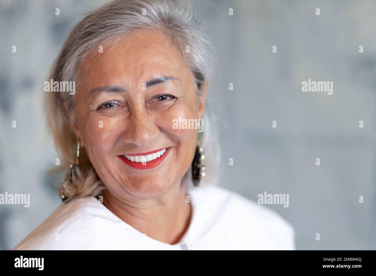 Donna dai capelli grigi con trucco luminoso guarda la macchina fotografica e ride Foto Stock